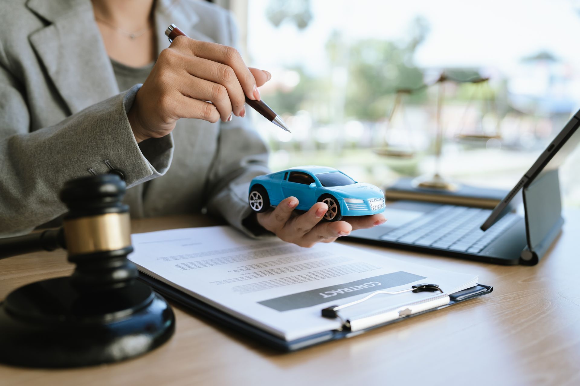 A lawyer holds a blue toy car and a pen while sitting inside an office.