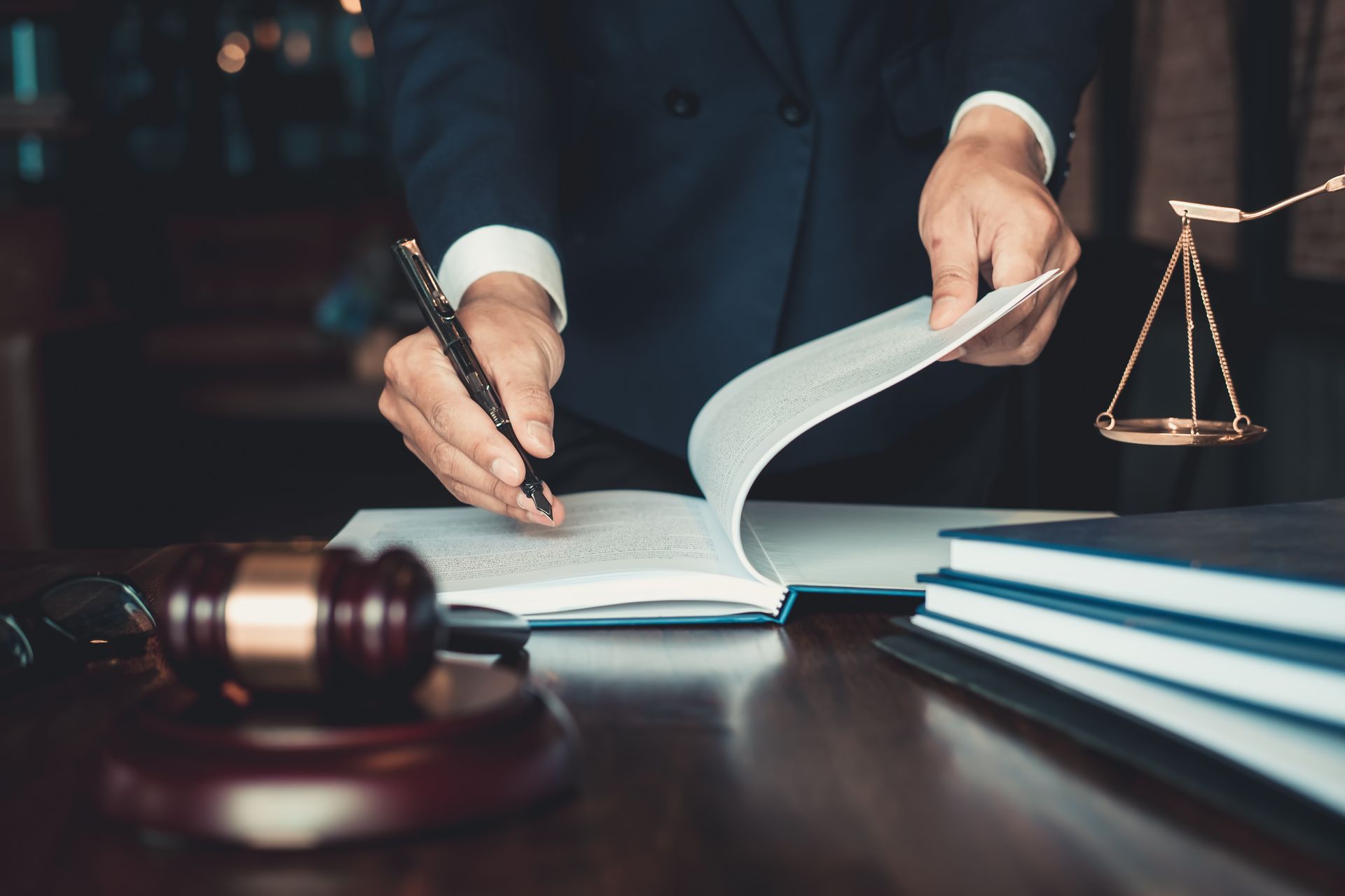 A person in a suit writes in a book near a wooden gavel and scales of justice, representing a legal professional at work.