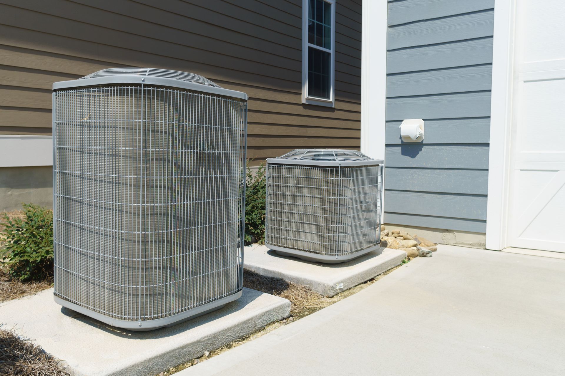 Two air conditioners are sitting outside of a house.