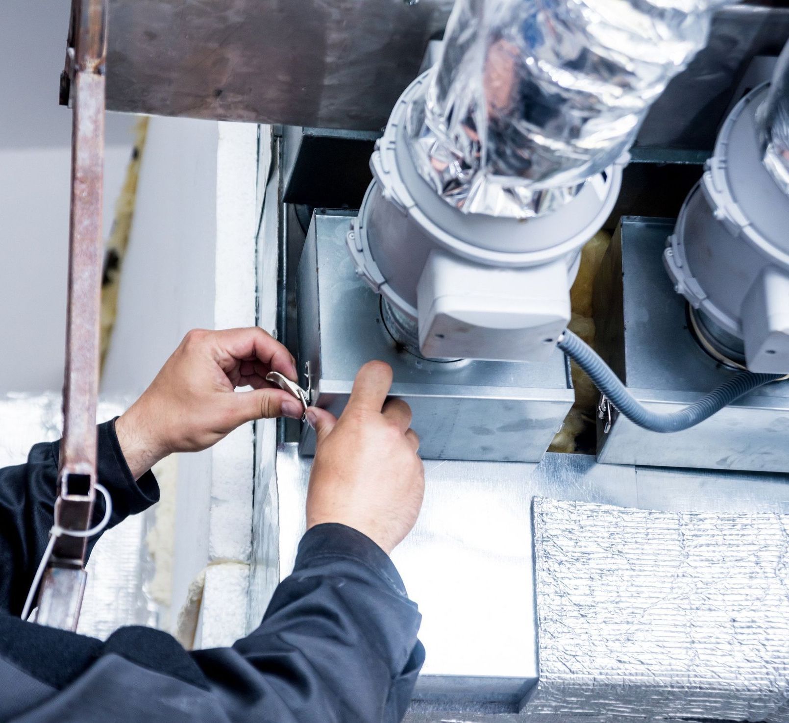 A man is working on a ventilation system in a building.