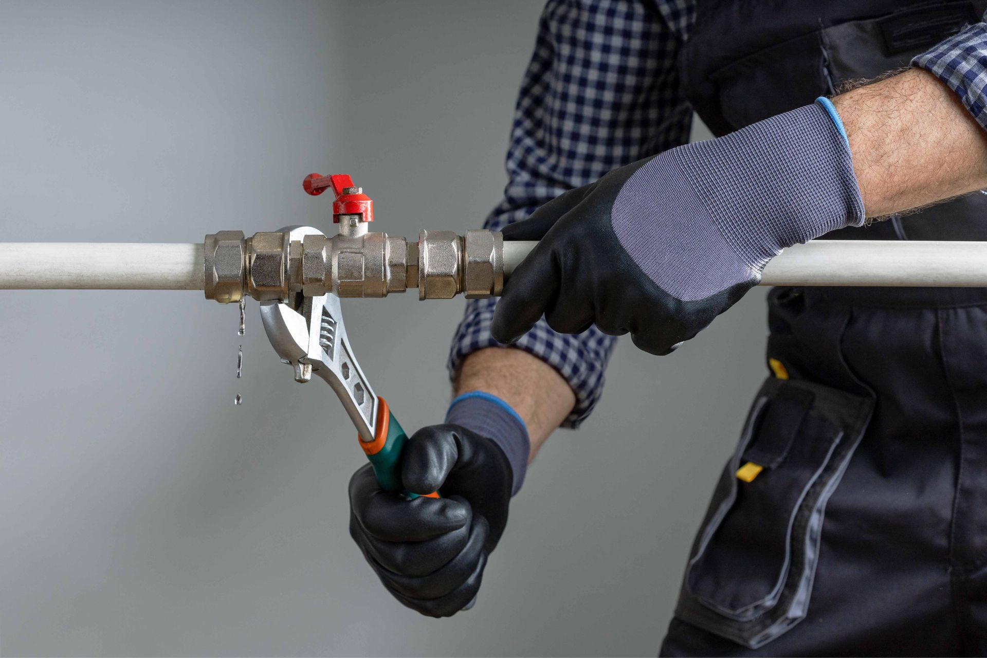 A worker wearing black work gloves uses an adjustable wrench to tighten a leaking metal pipe valve.