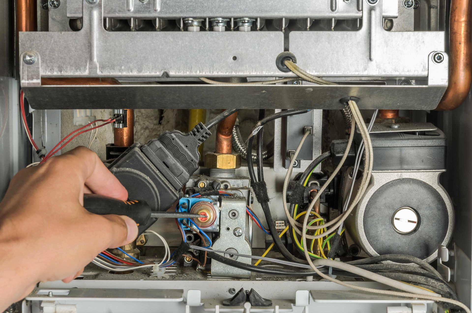 A close-up view of a hand using a screwdriver to adjust a brass valve on the internal components of a gas boiler.
