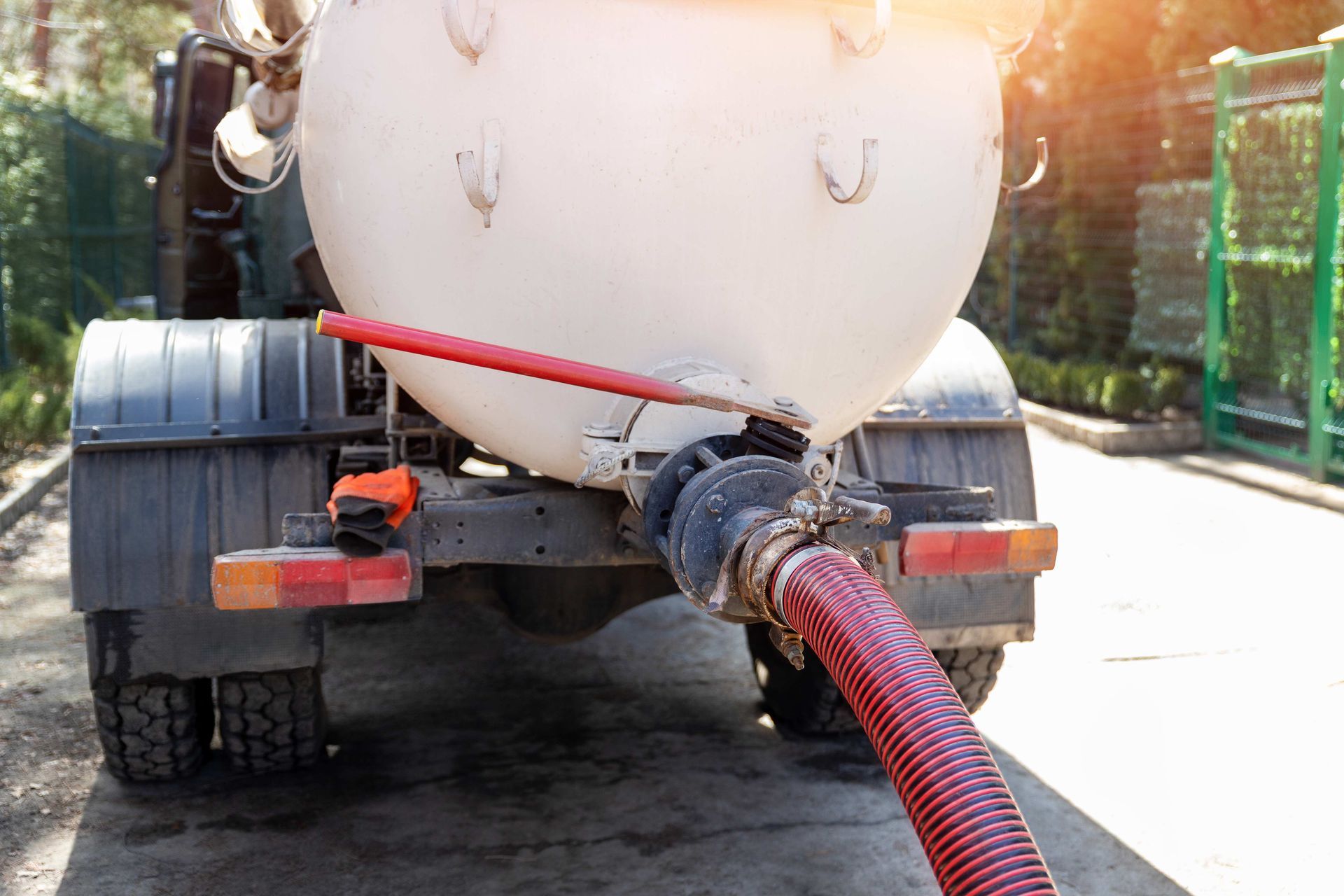 A close-up view of the rear of a white tanker truck with a red hose connected to a discharge valve.
