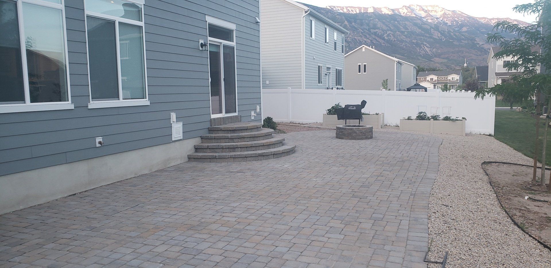 The backyard of a house with a brick patio and stairs leading up to it.