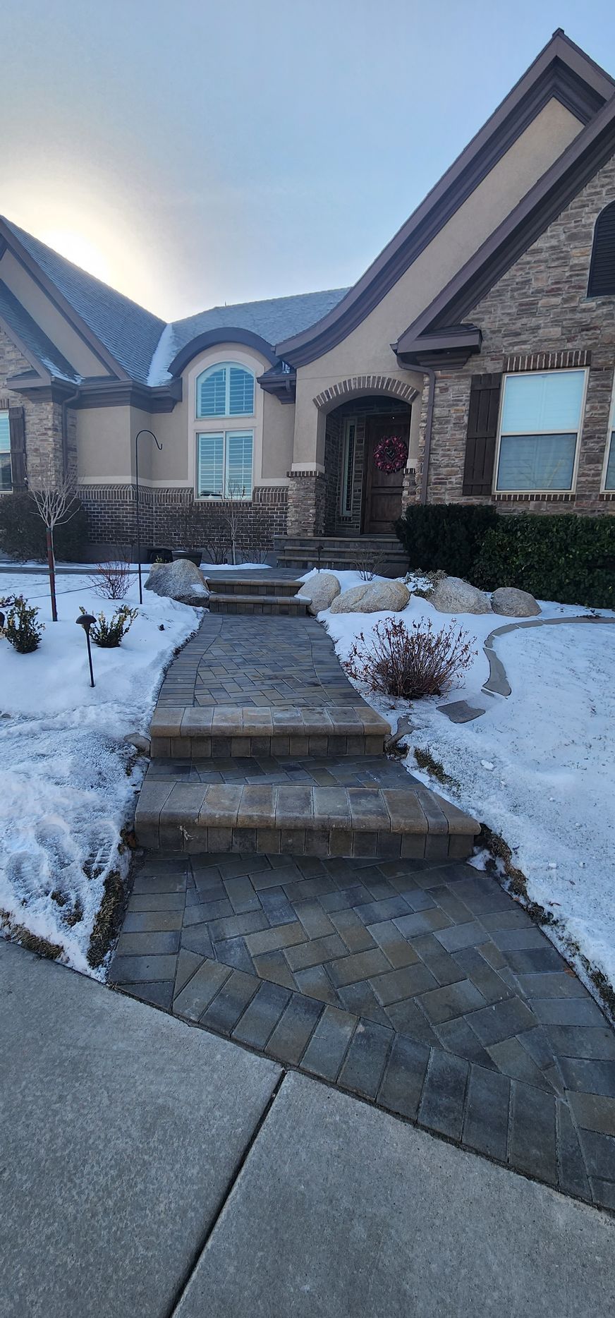 A brick walkway leading to a large brick house covered in snow.