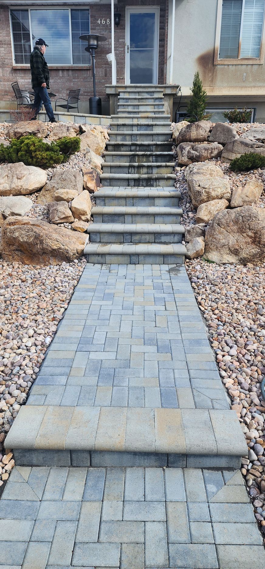 A man is walking down a stone walkway with stairs leading up to a house.