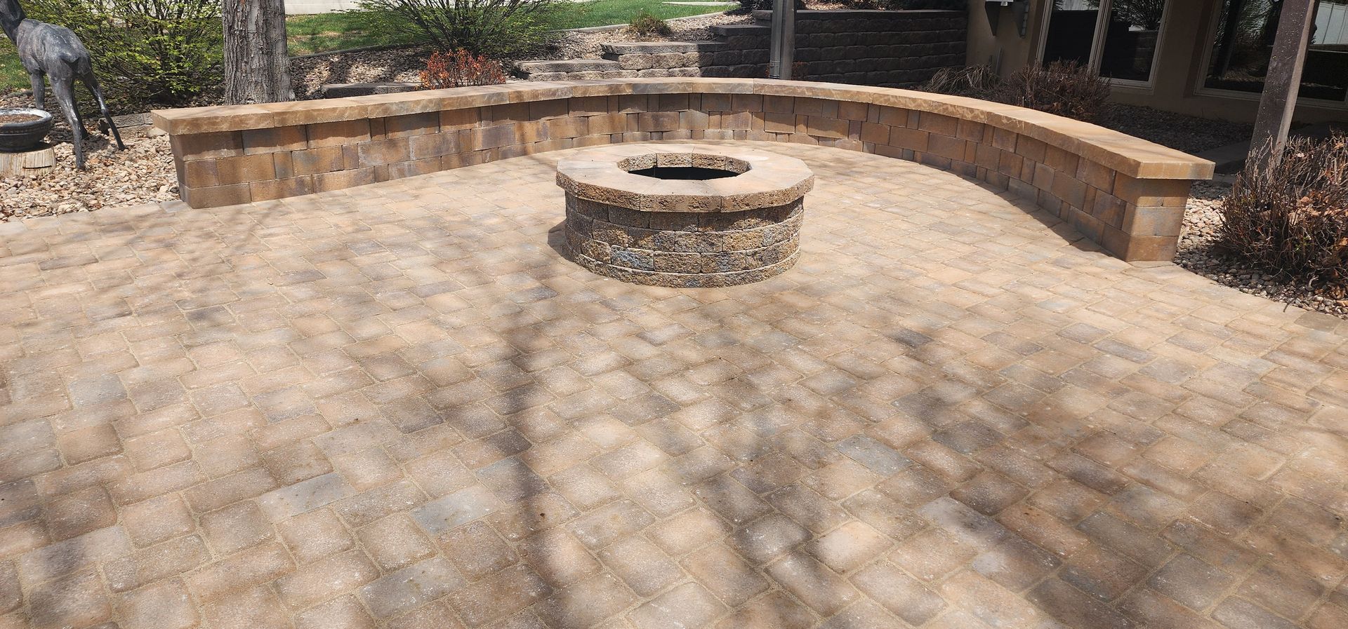 A fire pit is sitting in the middle of a patio next to a stone wall.