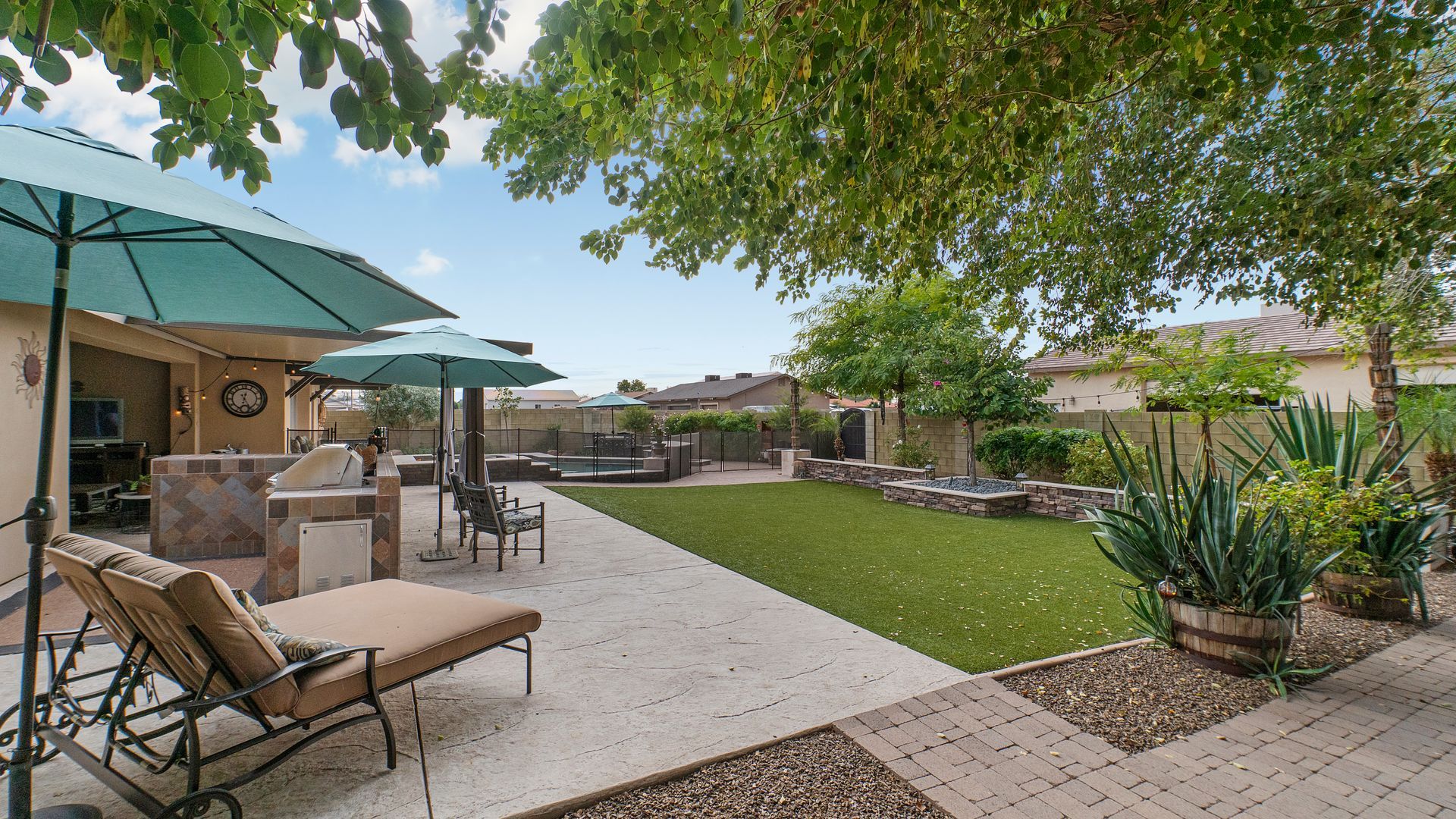 Concrete patio with outdoor seating, umbrellas, lawn, and landscaped backyard