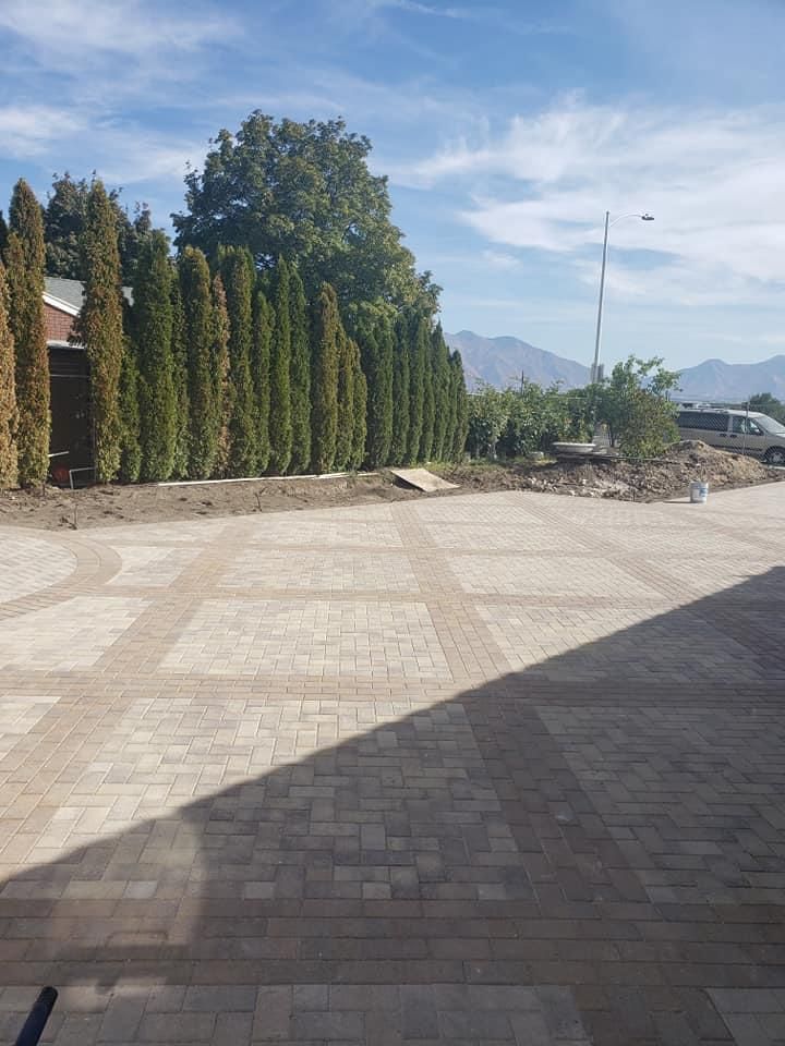 A brick driveway with a fence and trees in the background