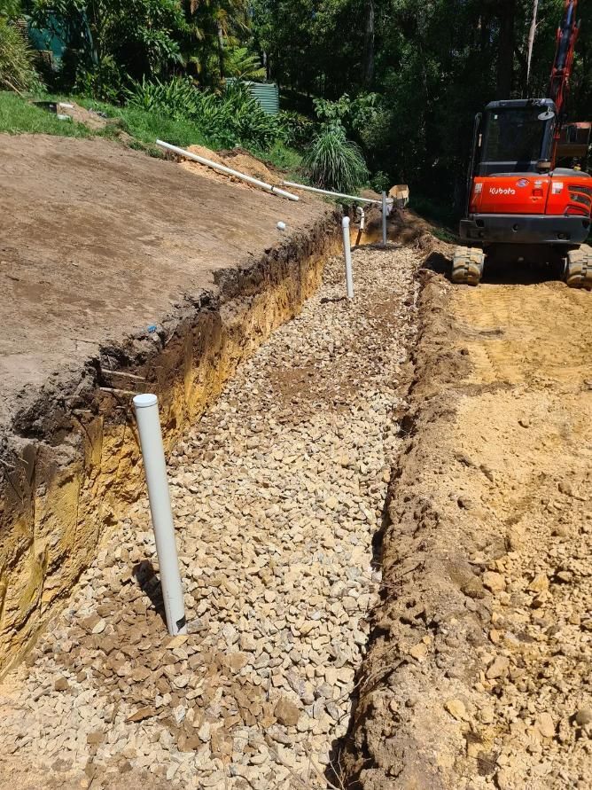 A Red Excavator Is Digging a Trench in The Dirt — Murwillumbah District Plumbing Service in Pottsville, NSW