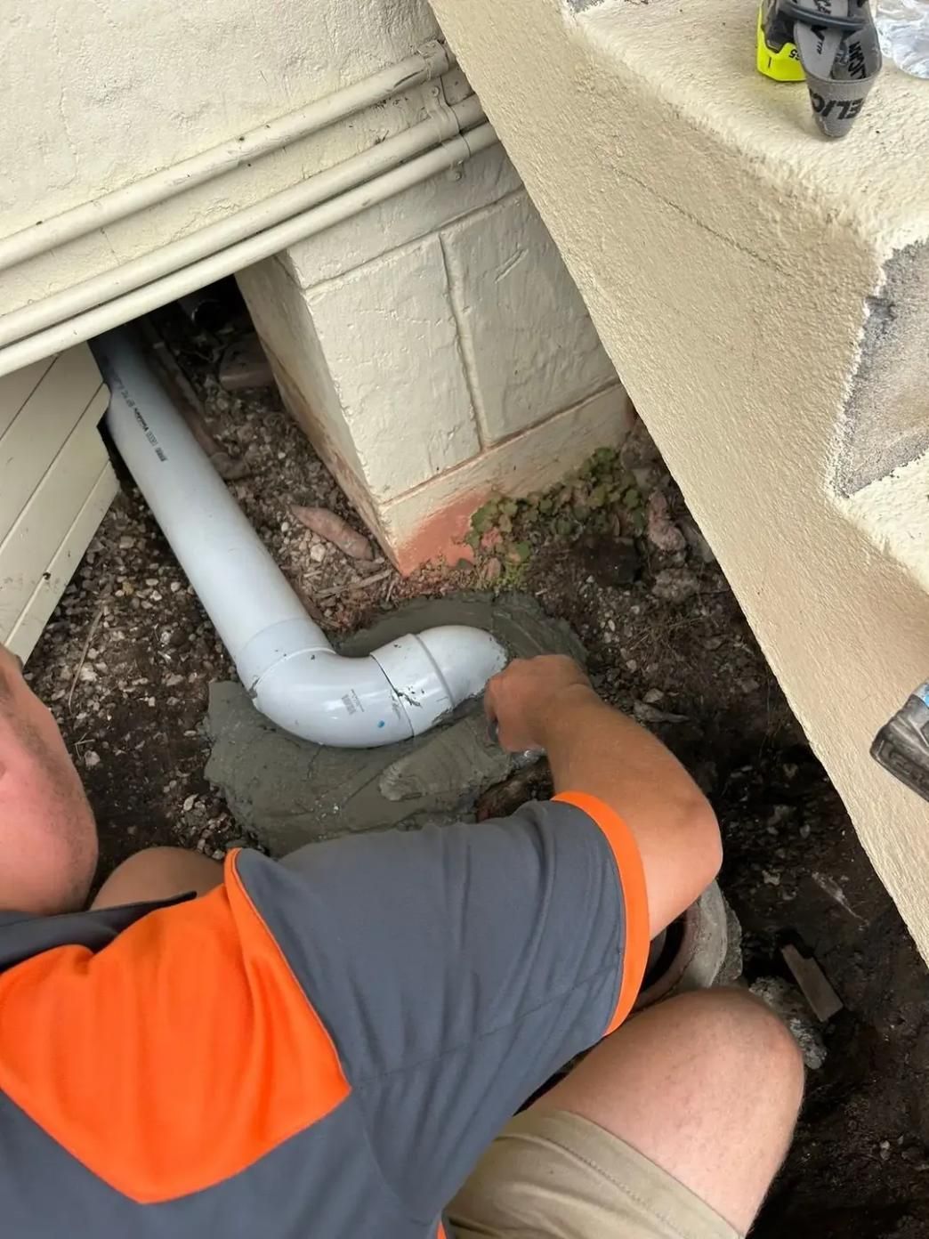 A Man Is Kneeling Down in The Dirt Working on A Pipe — Murwillumbah District Plumbing Service in Nunderi, NSW