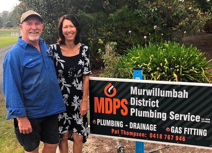 A Man and Woman Standing in Front of A Sign for Murwillumbah District Plumbing Services — Murwillumbah District Plumbing Service in Nunderi, NSW