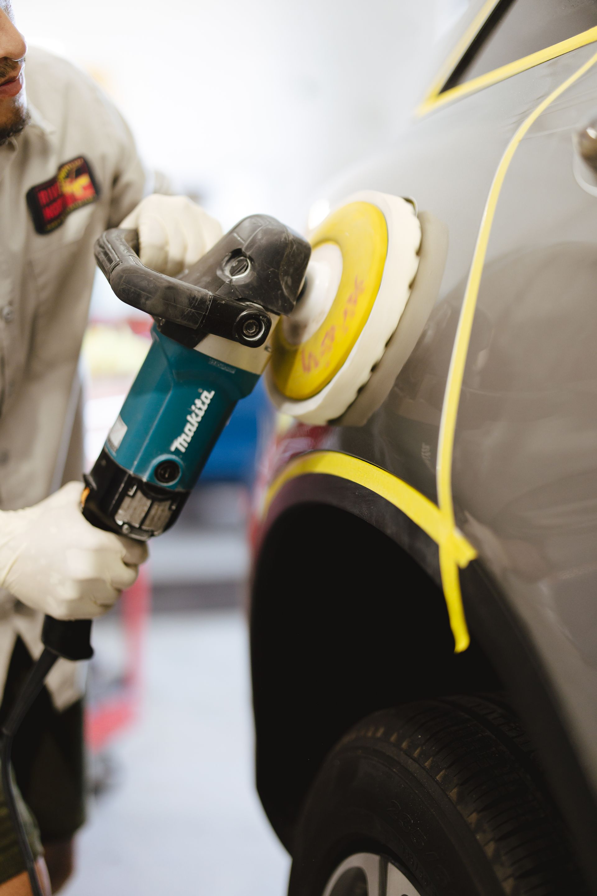 A man is sitting on a stool working on a car in a garage.
