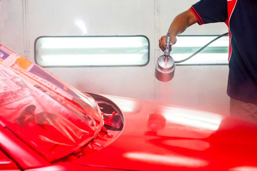 A man is spray painting a red car in a paint booth.