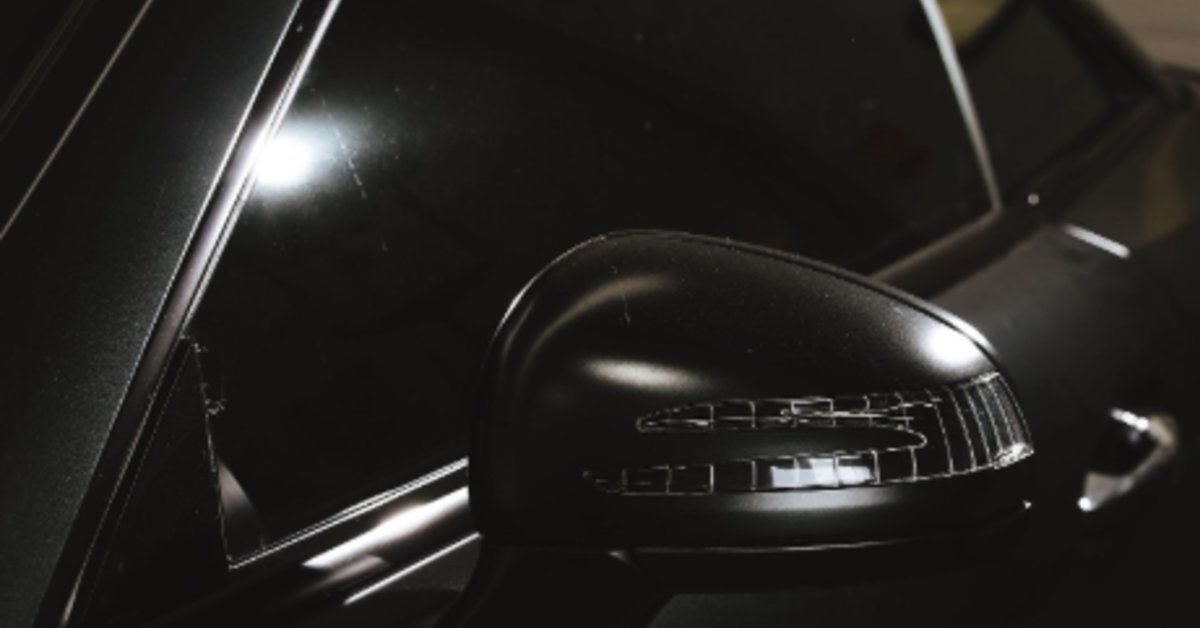 A close-up of a black car's side mirror and tinted window with bright reflections against a dark bac