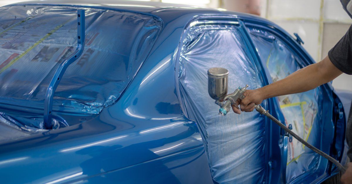 A worker painting the exterior of a car blue. Inside the car, the area is sealed to prevent paint fr