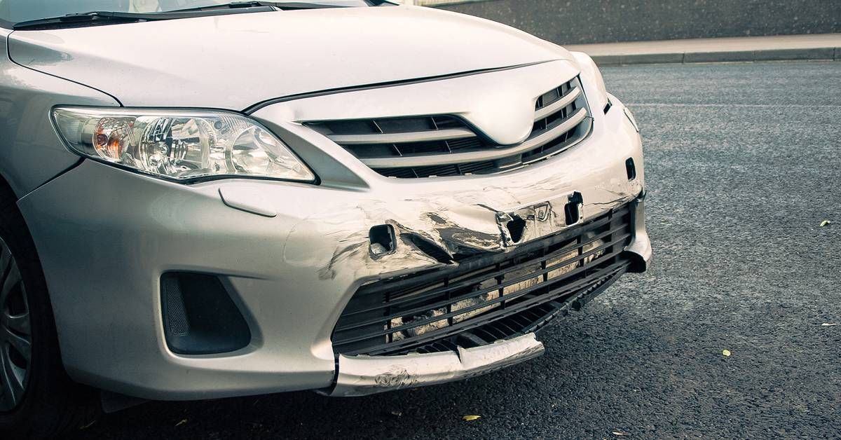 The front of a vehicle with damage to the bumper. There are scrapes, and part of the bumper is missi