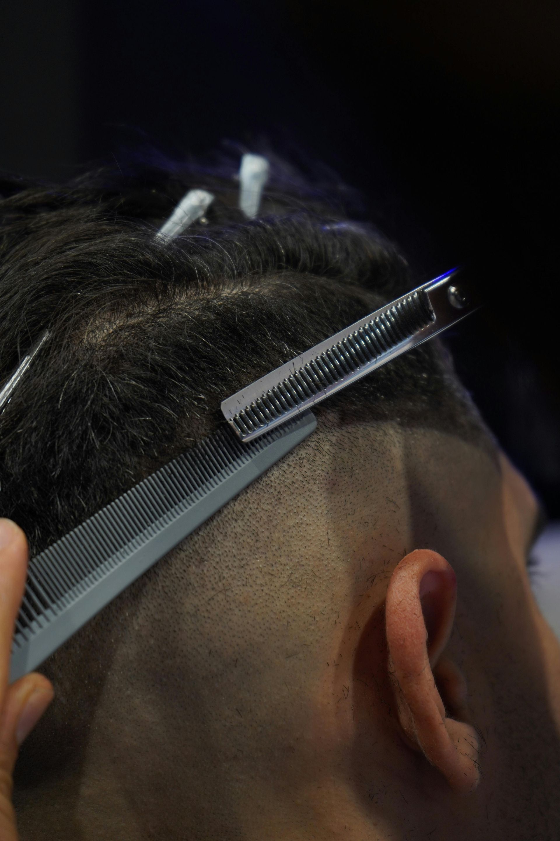 Barber using a straight razor to shave a fade haircut on a client's head.