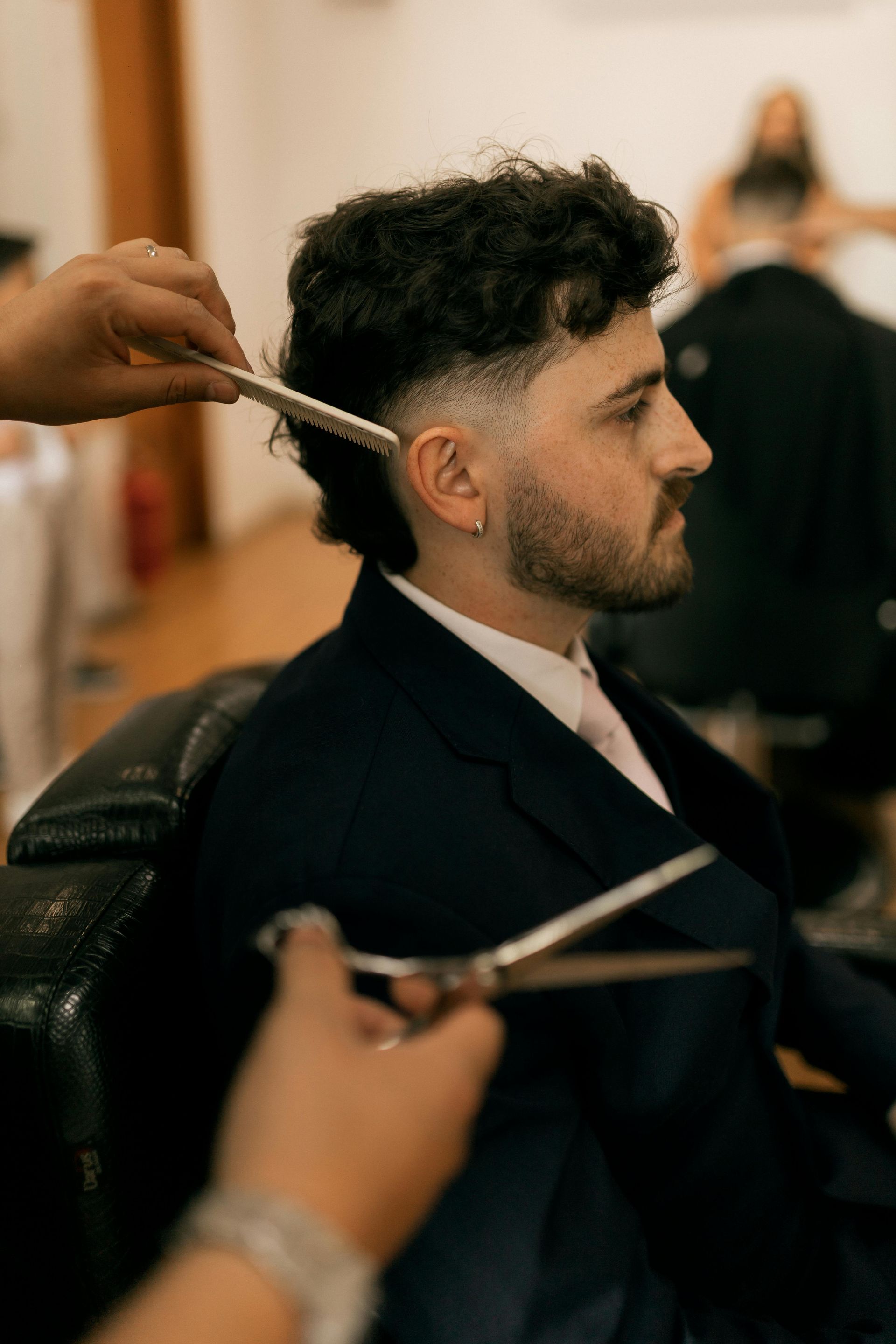 Man getting a haircut at a barbershop. The barber uses scissors and a comb.