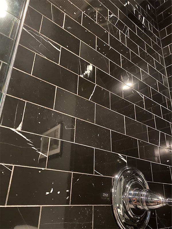 A bathroom with black tiles and a chrome shower head.