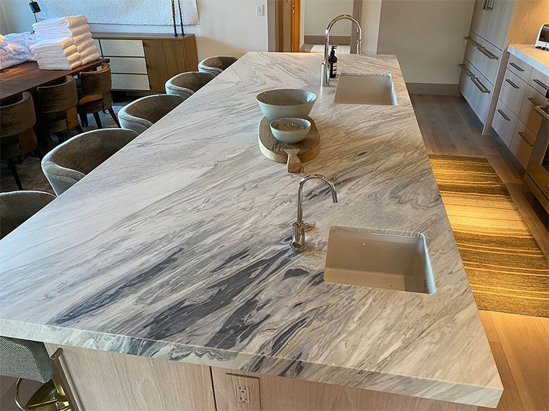 A kitchen with a marble counter top and two sinks.