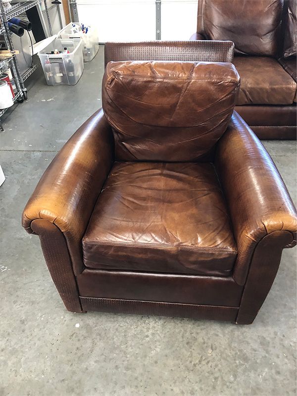 A brown leather chair is sitting on a concrete floor next to a couch.