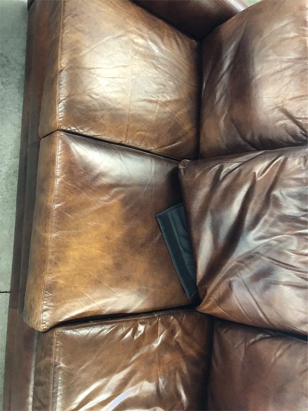 A close up of a brown leather couch with pillows