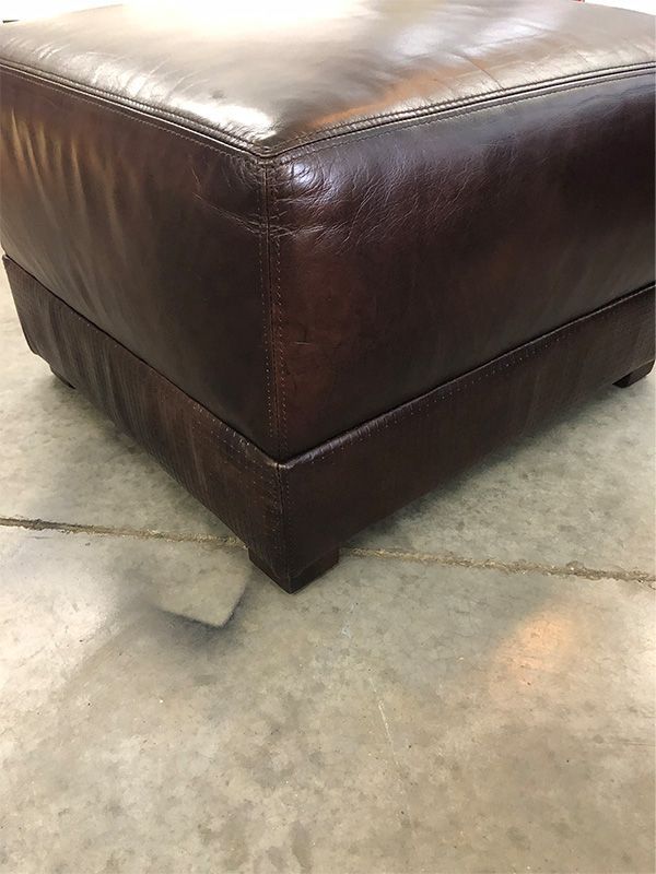 A brown leather ottoman is sitting on a concrete floor.