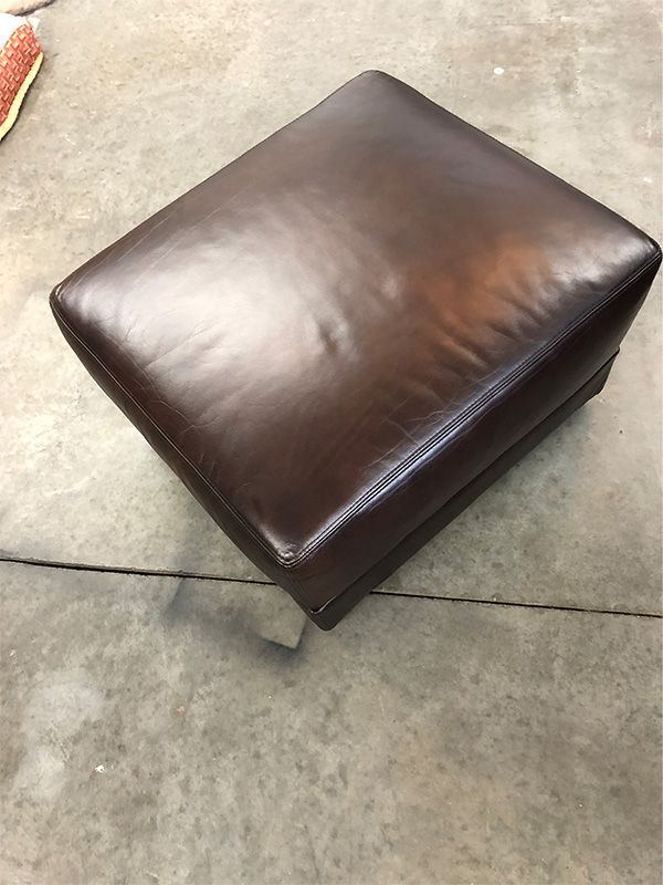 A brown leather ottoman is sitting on a concrete floor.