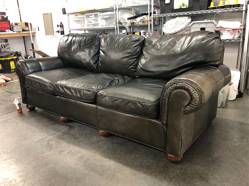 A black leather couch is sitting on a concrete floor in a room.