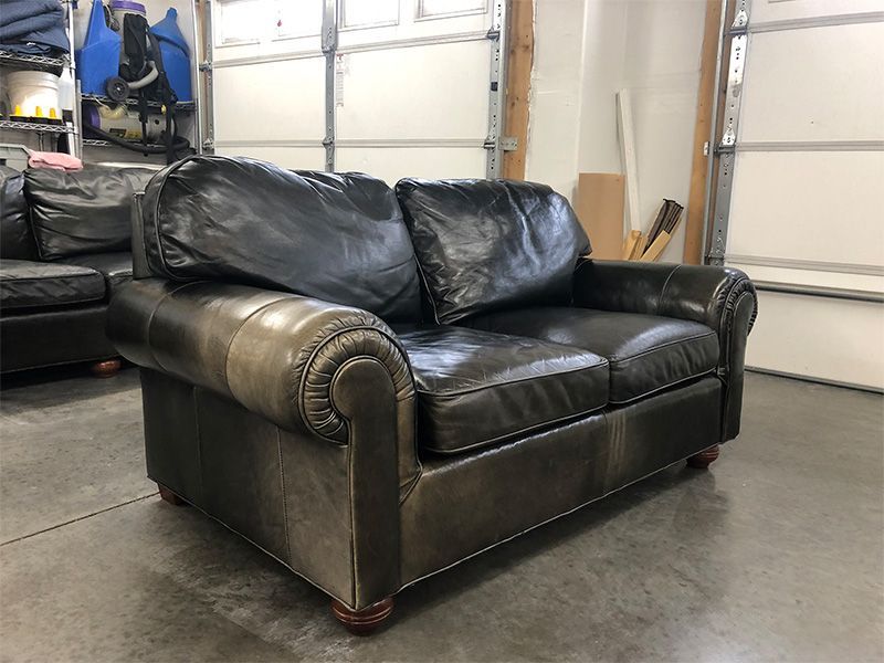 A black leather couch is sitting in a garage next to a garage door.
