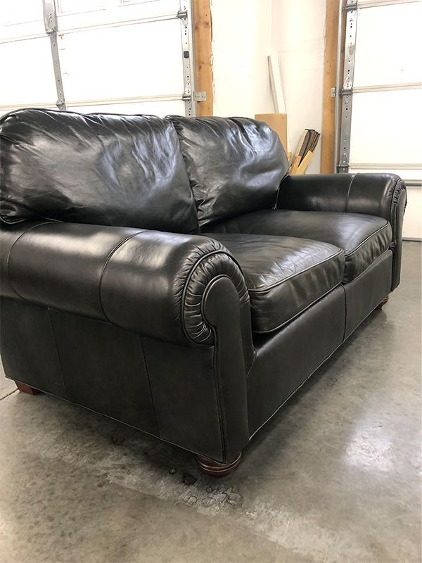 A black leather couch is sitting on a concrete floor in a garage.