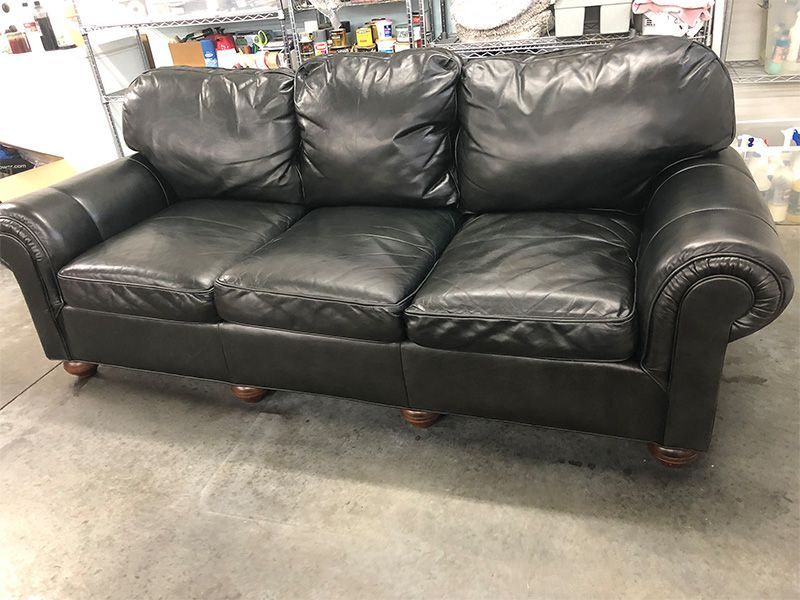 A black leather couch is sitting on a concrete floor in a room.