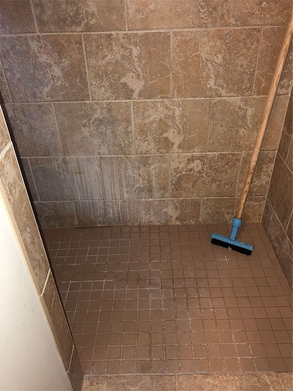 A blue broom is sitting in a tiled shower stall.