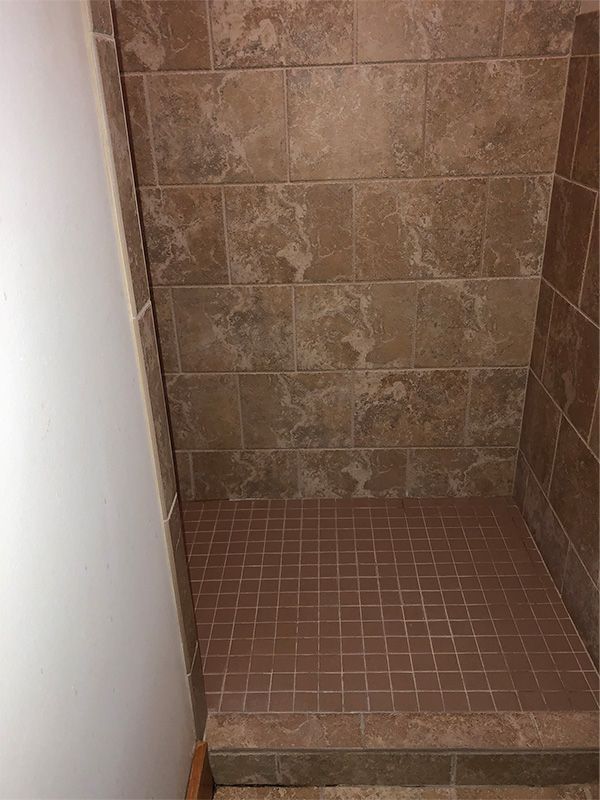 A walk in shower with brown tiles on the wall and floor.