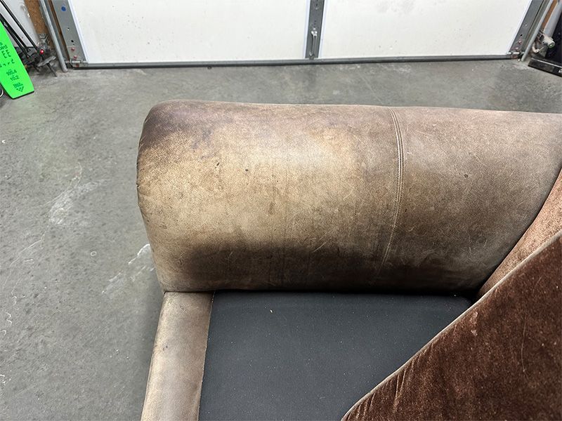 A brown leather couch is sitting in front of a garage door.