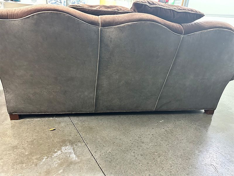 A brown leather couch is sitting on a concrete floor.