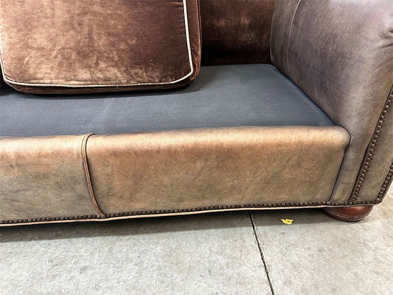 A brown leather couch is sitting on a concrete floor