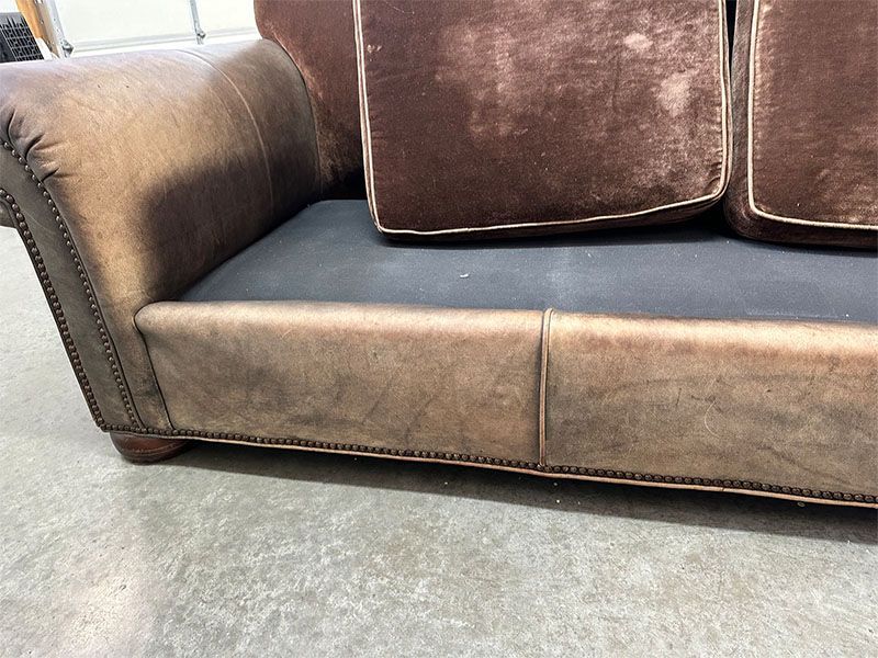 A brown leather couch is sitting on a concrete floor.