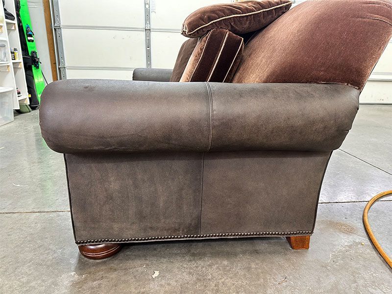 A brown leather couch is sitting on a concrete floor in a garage.