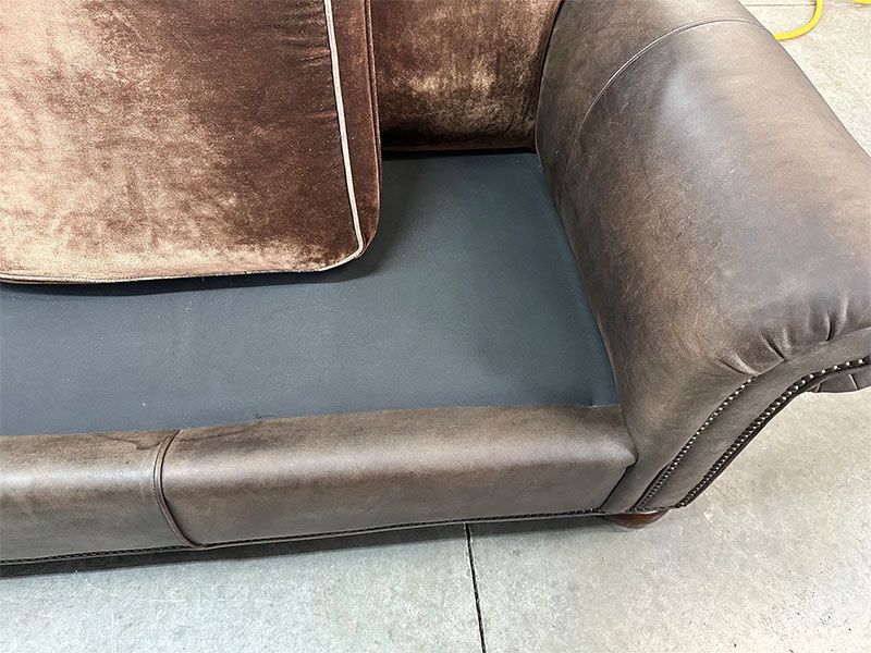 A brown leather couch is sitting on a concrete floor.