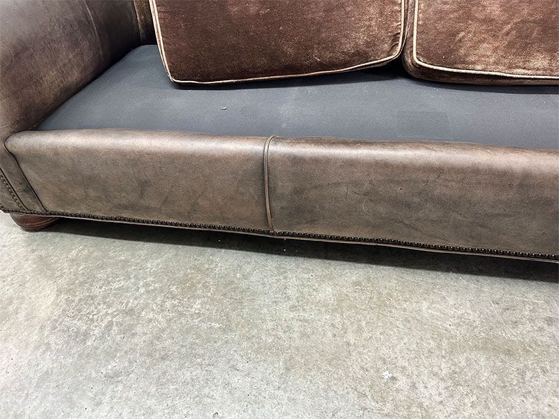A brown leather couch is sitting on a concrete floor.