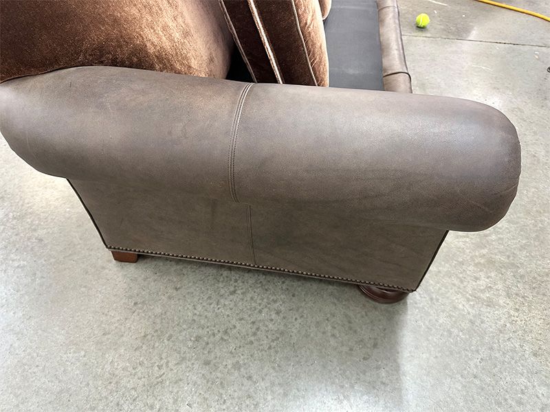 A brown leather couch is sitting on a concrete floor.