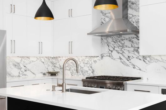 A kitchen with white cabinets , a stove , a sink , and a hood.