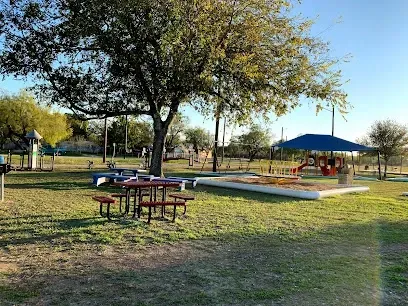 A picnic area in a park with tables and benches under a tree.