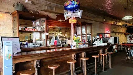A long wooden bar with stools in a restaurant with a birthday balloon hanging from the ceiling.