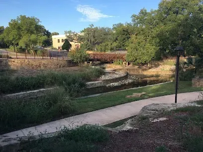 A path leading to a bridge over a river in a park.