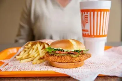 A woman is sitting at a table eating a chicken sandwich and french fries.