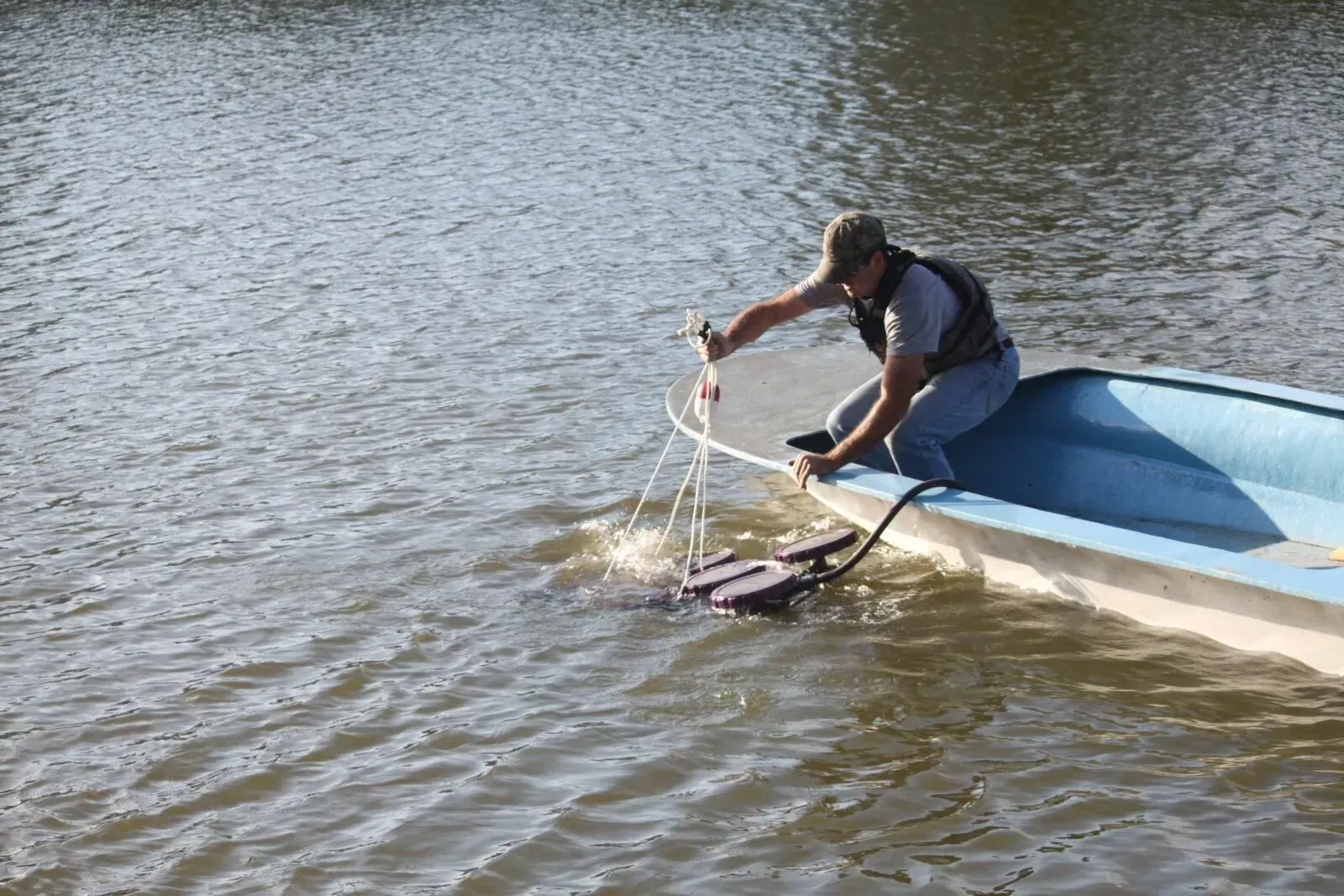 Two people on a small motorized board skimming across a pond, with trees and grassy shore behind them.