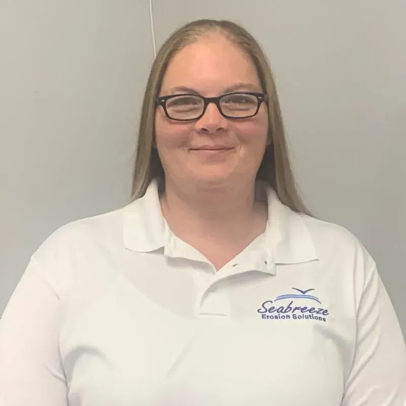 Woman in glasses wearing a white Seaside vacation services polo, standing against a gray background